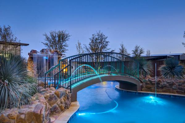 Bridge with evening lights, spanning custom swimming pool in custom-built home near Lubbock.